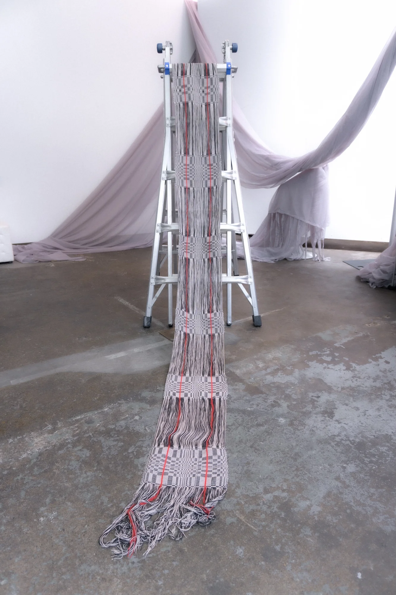 Long woven textile displayed on a sculptural frame